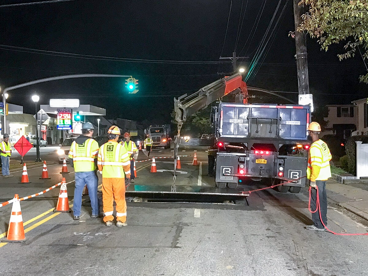 Night utility crew placing a steel road plate during emergency restoration work